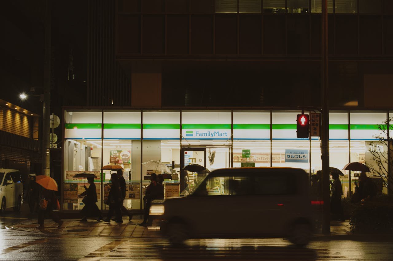 People crossing a street near a FamilyMart in Japan during a rainy night.